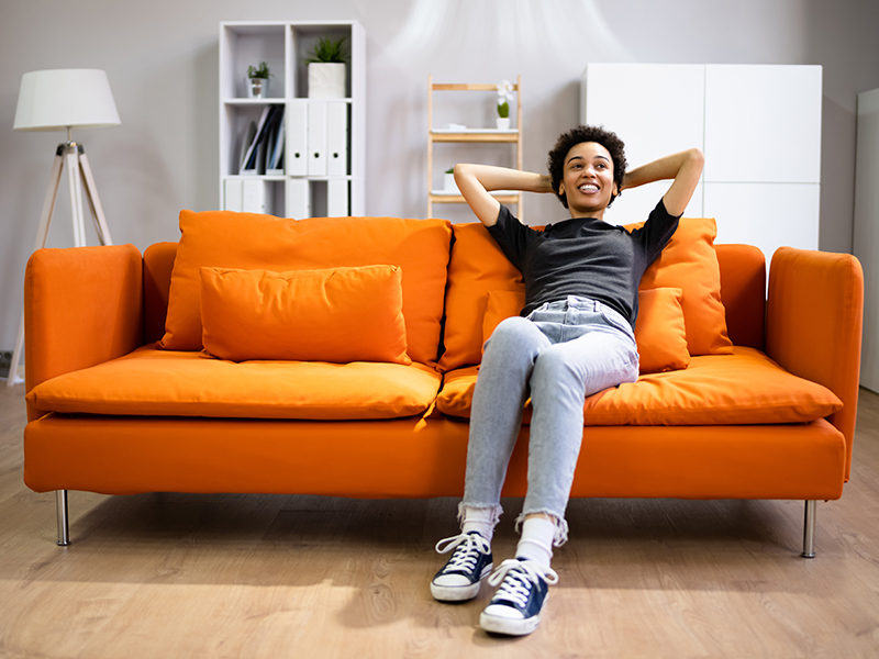 Kvinna som sitter bakåtlutad i en orange soffa i ett ljust rum.