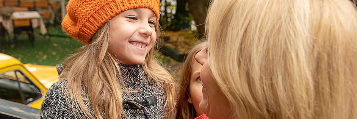 Mamma med två döttrar som ler mot varandra.