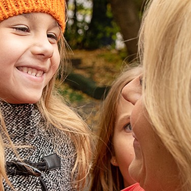 Mamma med två döttrar som ler mot varandra.
