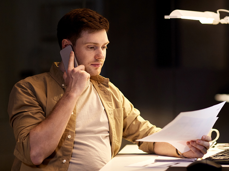 En man sitter vid ett skrivbord, talar i telefonoch håller i en faktura.