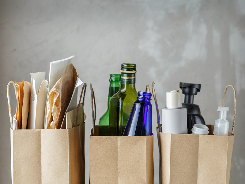 Tre bruna kassar som innehåller papper, glasflaskor och plastflaskor.