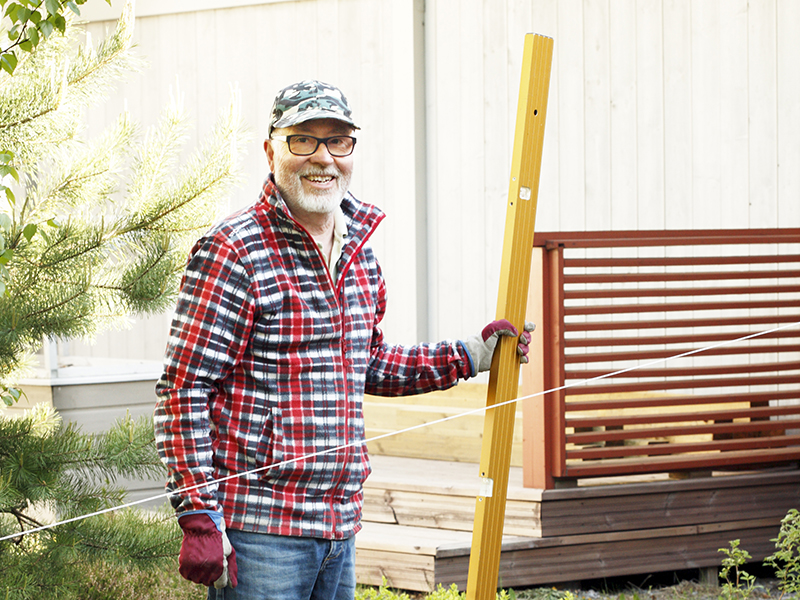 Man som står vid sin uteplats och håller ett vattenpass i ena handen.