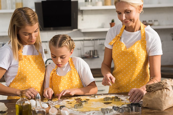 En mamma, en dotter och en mormor bakar kakor i ett kök.